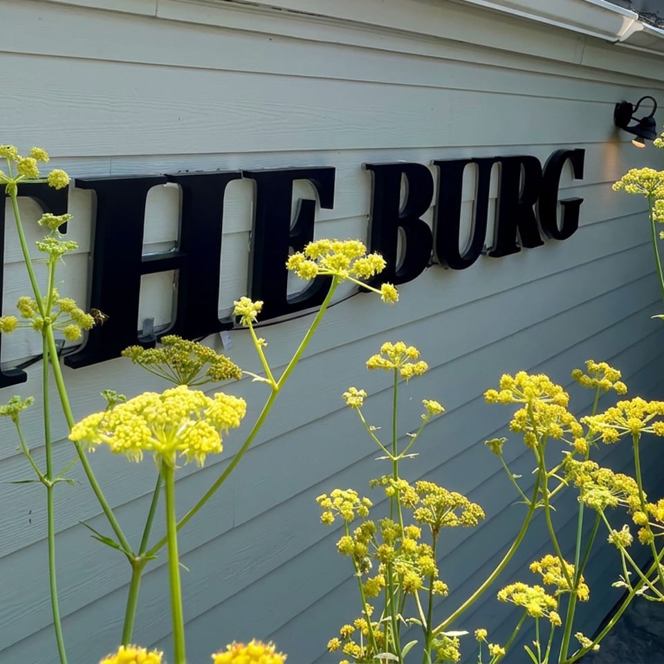 Yellow flowering plants frame large black THE BURG lettering on a light-sided restaurant exterior.